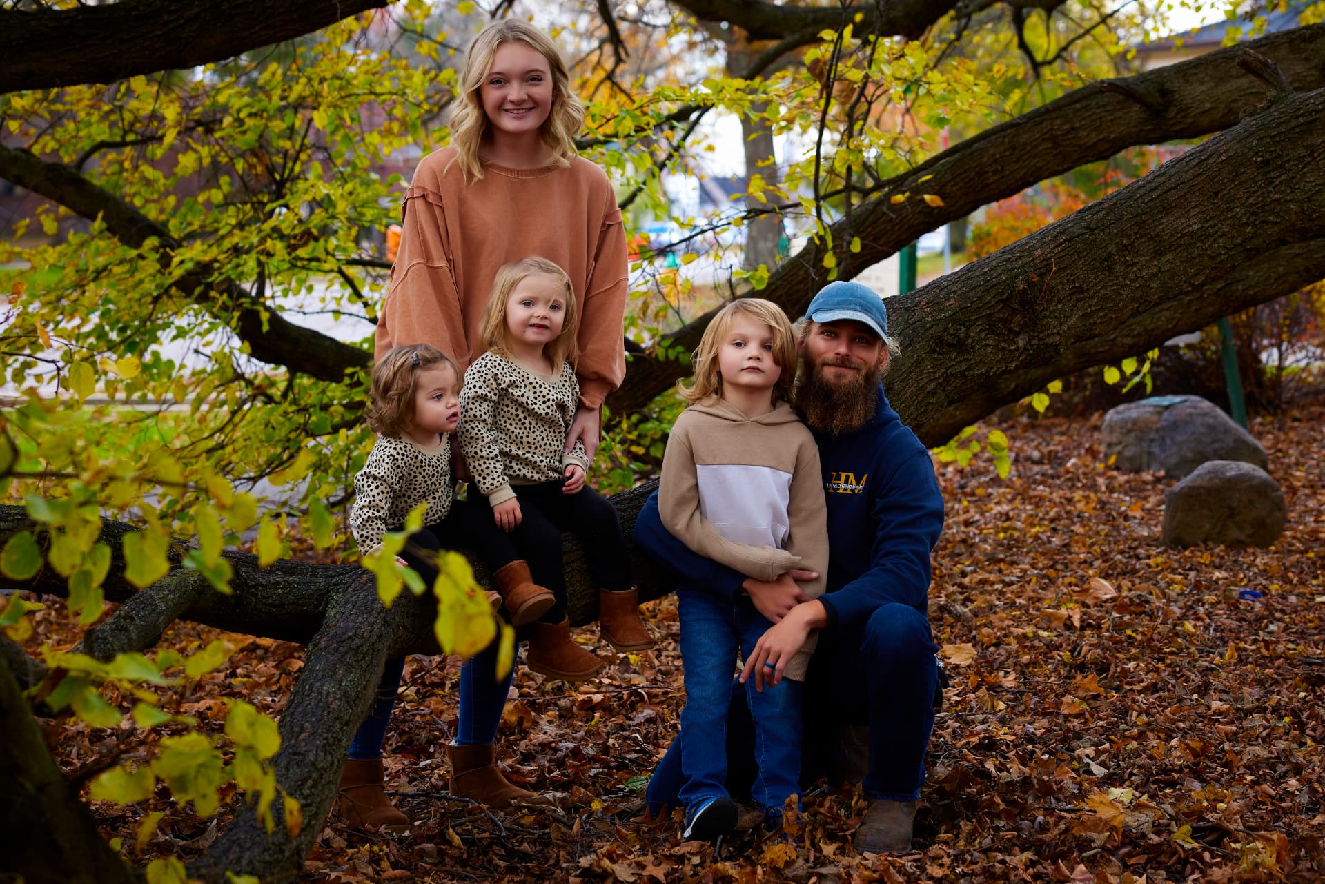 Family of five on a fallen tree branch among autumn leaves, Central Illinois family photographer
